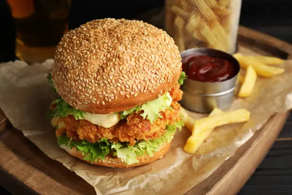 Delicious burger with crispy chicken patty, french fries and sauce on table, closeup