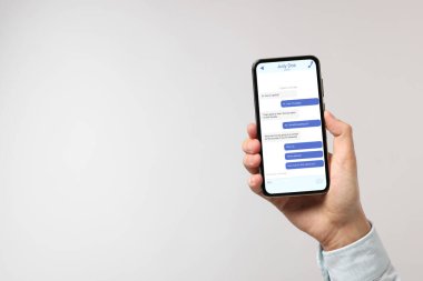 Arkadaşlarıyla mesajlaşan bir adam akıllı telefondan açık gri arka plana mesaj yolluyor, yakın plan. Metin için boşluk
