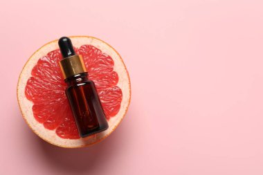 Bir şişe greyfurt yağı ve pembe arka planda taze meyve. Metin için boşluk