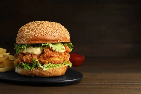 Delicious burger with crispy chicken patty on wooden table. Space for text