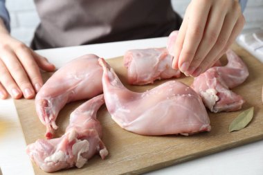 Beyaz ahşap masada çiğ tavşan etine tuz koyan kadın, yakın plan.