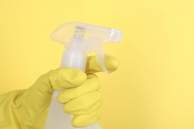 Sarı arka planda plastik sprey şişesi tutan kadın, yakın plan. Metin için boşluk