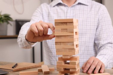 Jenga oynuyorum. Kapalı alandaki masadaki ahşap bloğu kuleden kaldıran adam.