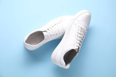 Açık mavi arka planda bir çift şık beyaz spor ayakkabı.