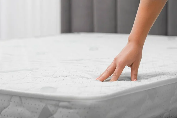 Woman touching new soft mattress indoors, closeup
