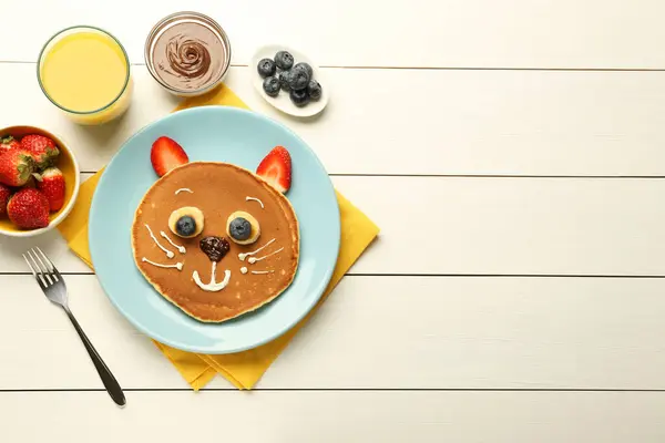 Creative serving for kids. Plate with cute cat made of pancakes, berries, cream, banana and chocolate paste on white wooden table, flat lay. Space for text