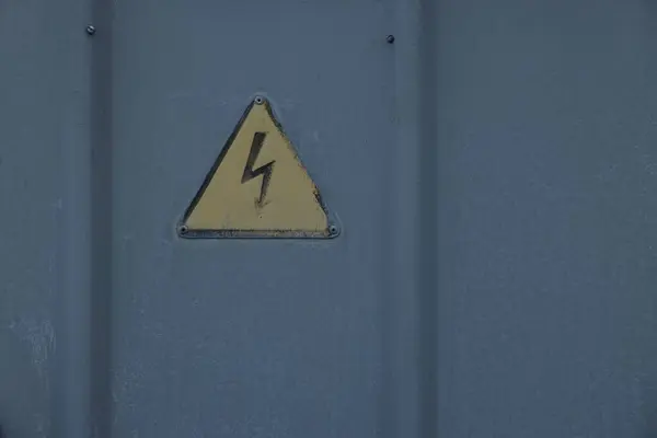 Yellow high voltage sign on grey metal surface. Space for text