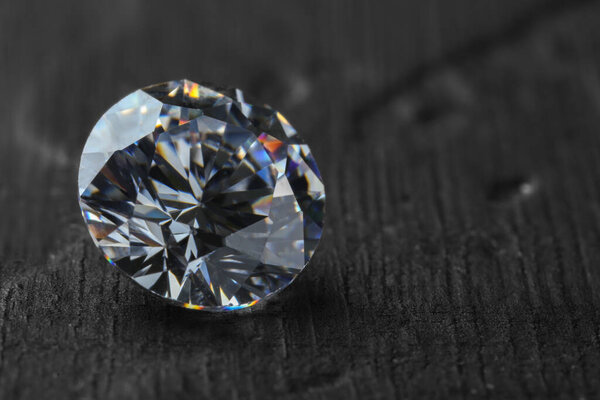 Beautiful shiny diamond on dark gray table, closeup. Space for text