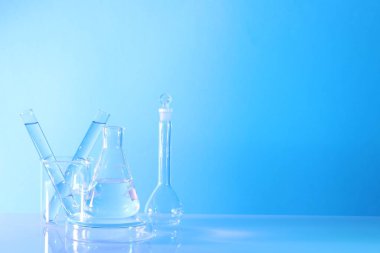 Laboratuvar analizi. Masada açık mavi arkaplana karşı farklı cam eşyalar