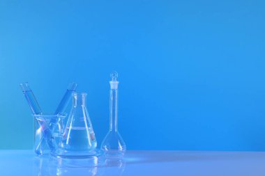 Laboratuvar analizi. Masada açık mavi arkaplana karşı farklı cam eşyalar