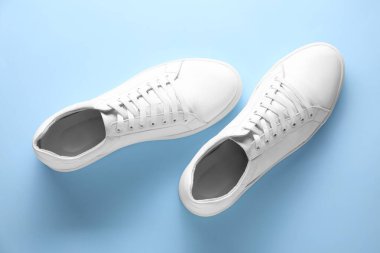 Açık mavi arka planda bir çift şık beyaz spor ayakkabı.