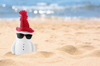 Güneş gözlüklü, kumlu sahilde kırmızı şapkalı şirin, küçük bir kardan adam.
