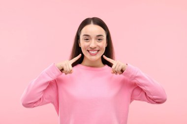 Güzel bir kadın temiz dişlerini gösteriyor ve pembe arka planda gülümsüyor.