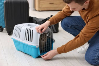Evcil hayvanla seyahat et. Evde kedisi olan bir adam taşıyıcıyı kapatıyor.
