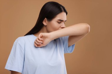 Kahverengi arka planda öksüren bir kadın. Soğuk belirtileri