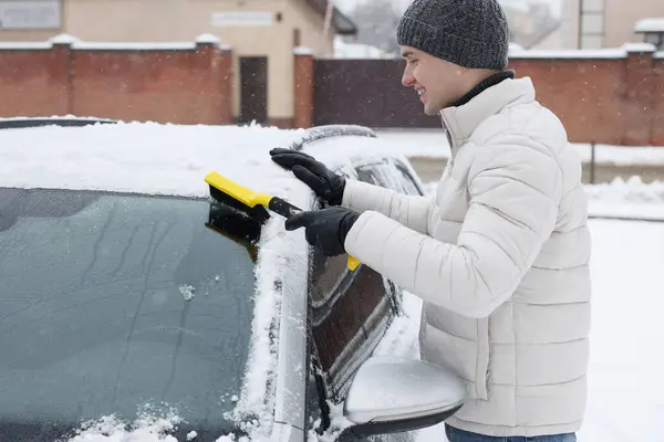 Man cleaning snow from car windshield outdoors