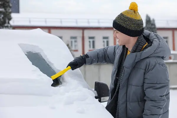 Man cleaning snow from car windshield outdoors
