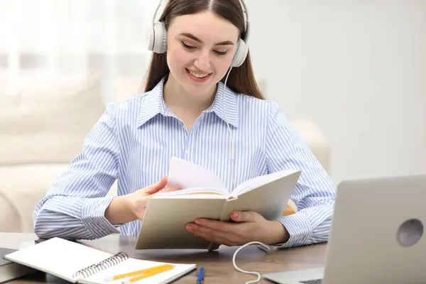E-learning. Young woman with book during online lesson at table indoors