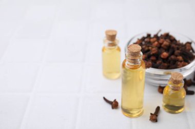 Şişelerdeki karanfil yağı ve beyaz döşeme masasındaki kurumuş tomurcuklarla dolu kase, metin için yer.