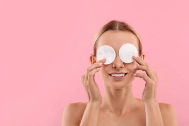 Gülümseyen kadın pembe arka planda pamuk pedlerle makyajı temizliyor. Metin için boşluk