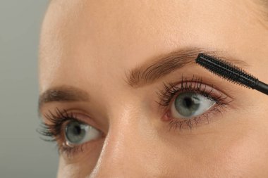 Gri arka plana rimel süren kadın, yakın plan.