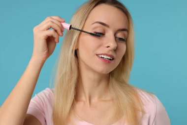 Açık mavi arka planda rimel süren güzel kadın, yakın plan.