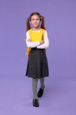 Sırt çantası ve menekşe arkaplan kitabıyla gülümseyen liseli kız