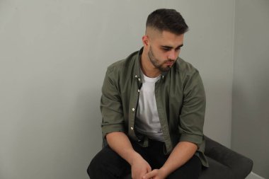 Üzgün adam açık gri duvarın yanında oturuyor. Metin için boşluk