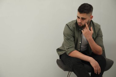 Üzgün adam açık gri duvarın yanında oturuyor. Metin için boşluk