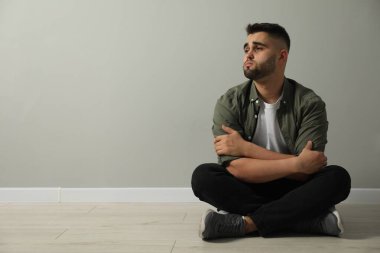 Açık gri duvarın yanında yerde oturan üzgün adam. Metin için boşluk