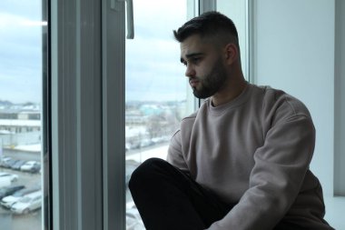 Evdeki pencereye bakan üzgün adam.