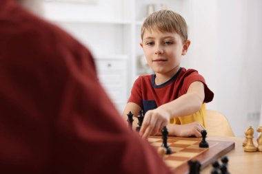 Küçük çocuk odada büyükbabasıyla satranç oynuyor.