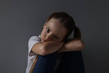 Koyu gri arka planda oturan üzgün kız