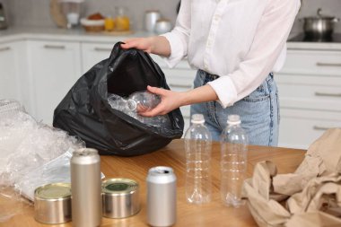 Çöp ayıklama. İçerideki ahşap masada plastik şişeyi çantaya koyan kadın, yakın plan.