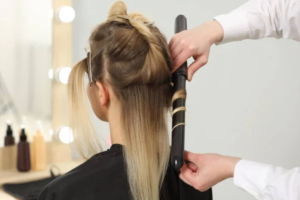 Hair styling. Hairdresser curling woman's hair in salon, closeup