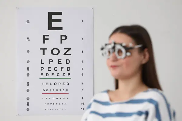 Young woman with trial frame against vision test chart, selective focus
