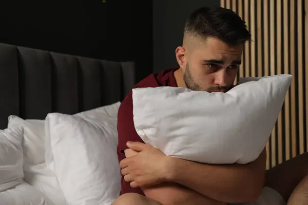 Sad man hugging pillow on bed at home. Space for text