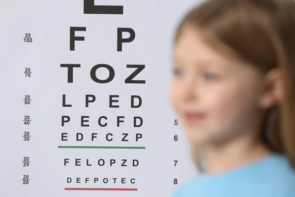 Cute little girl against vision test chart, selective focus