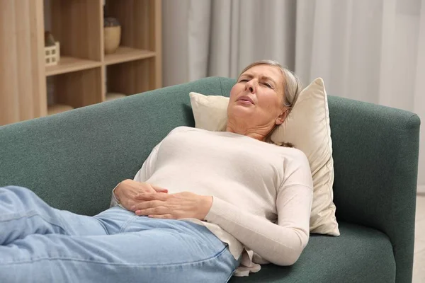 Menopause. Woman suffering from abdominal pain on sofa at home