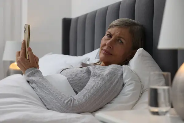 Menopause. Sleepless woman using smartphone in bed indoors
