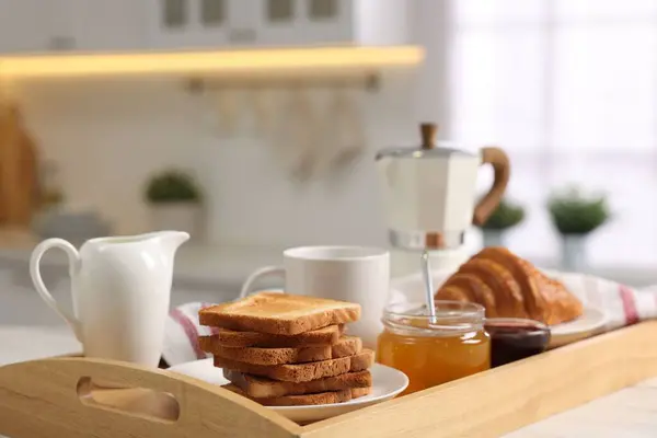 Breakfast served in kitchen. Tray with toasts, honey, jam, fresh croissant, coffee and pitcher of milk on white table, closeup