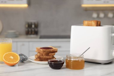 Kahvaltı için kadeh kaldırıyorum. Cihaz, çıtır ekmek, bal, reçel ve portakal. Mutfaktaki beyaz masada taze.