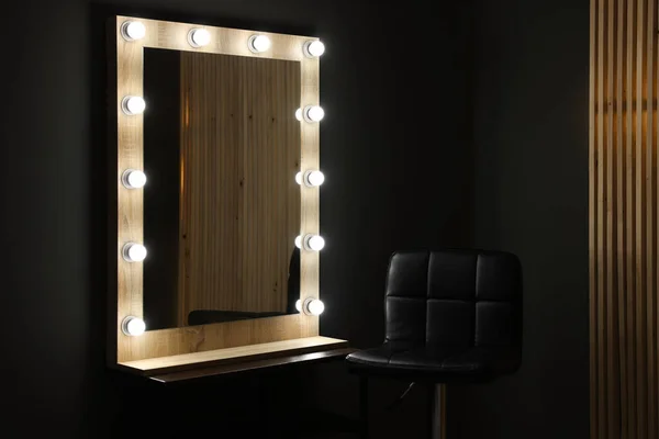 Beautiful mirror with light bulbs and chair in makeup room
