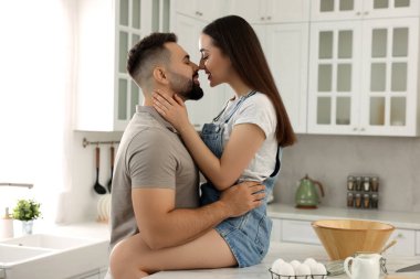 Şefkatli genç bir çift açık mutfakta öpüşüyor.