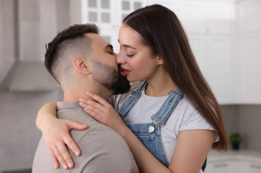 Şefkatli genç bir çift açık mutfakta öpüşüyor.