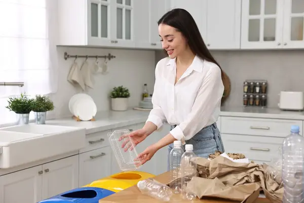 Smiling woman separating garbage in kitchen. Space for text