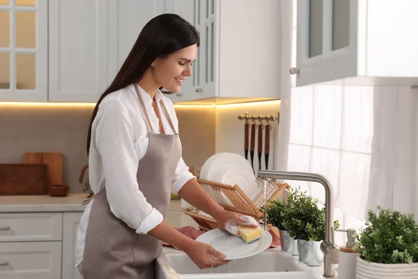 Happy woman washing plate at sink in kitchen