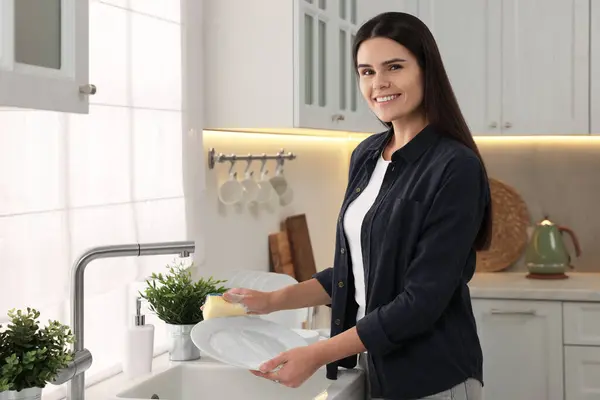 Happy woman washing plate at sink in kitchen