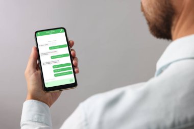 Arkadaşla mesajlaşan adam akıllı telefonda gri arkaplan üzerinde mesajlaşma uygulaması kullanıyor, yakın plan