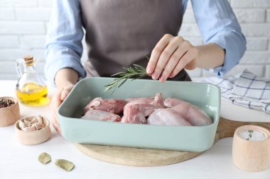 Beyaz ahşap masada çiğ tavşan etiyle biberiye pişiren kadın, yakın plan.